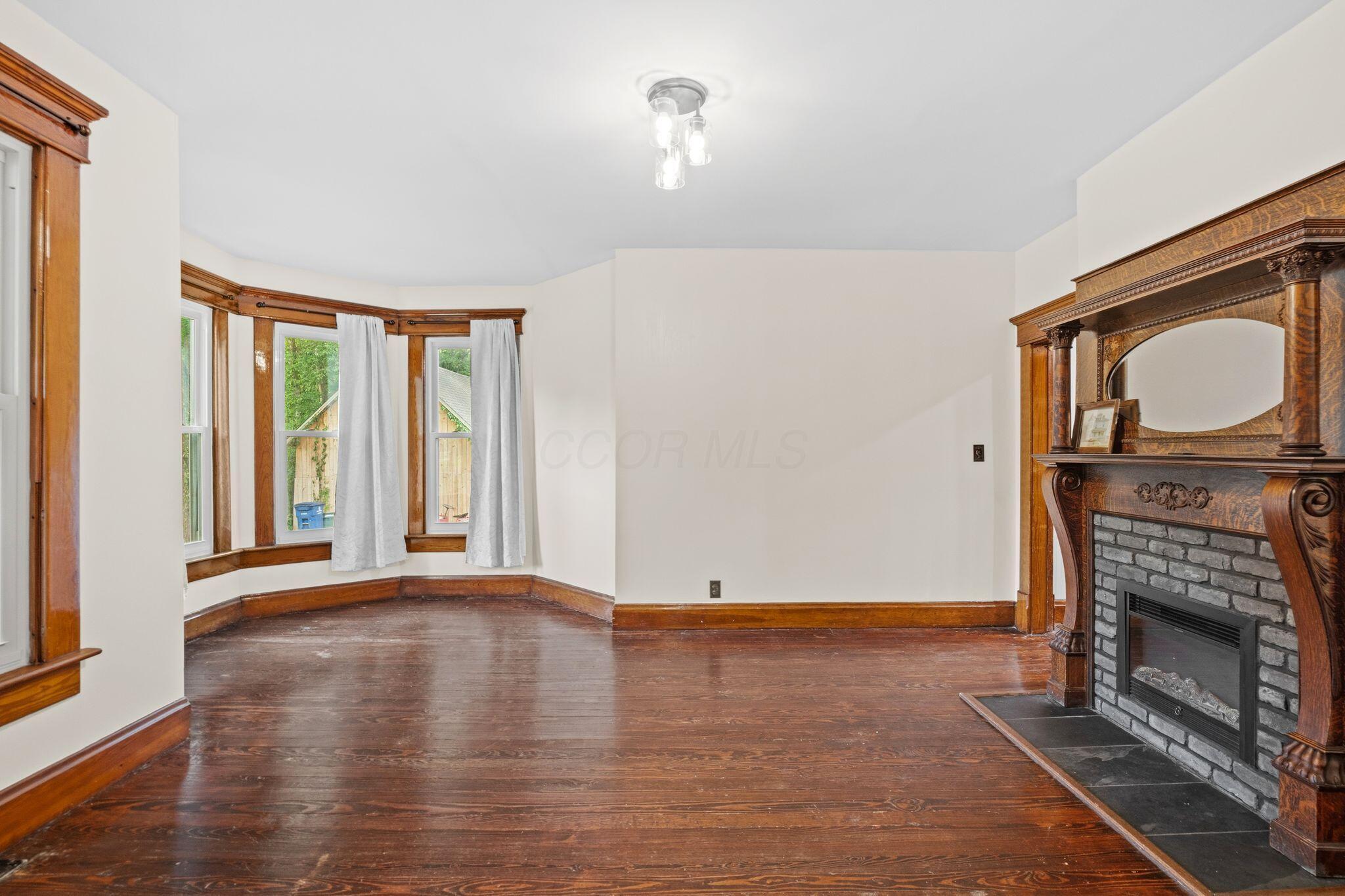 107 Price Road Columbus, OH 43230 - Photo 5 of 51 Spacious room featuring hardwood flooring, a decorative fireplace with an ornate wood mantel, and a bay window with natural wood trim