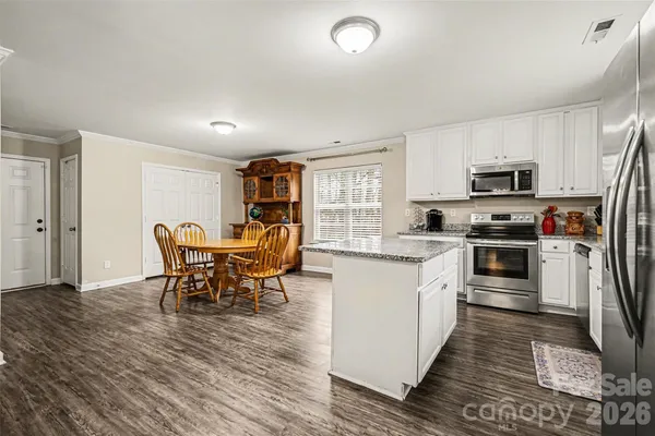 a kitchen with stainless steel appliances granite countertop a stove top oven a sink dishwasher a dining table and chairs with wooden floor