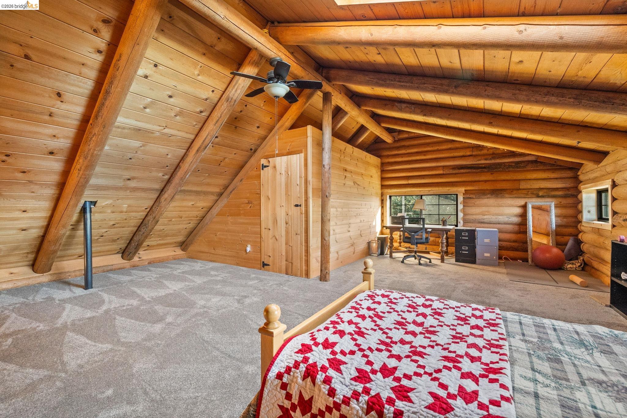 16144 Big Hill Road Sonora, CA 95370 - Photo 30 of 51 Vaulted log beam ceiling with a visible ceiling fan, light-toned wood plank walls, and light gray patterned carpeting