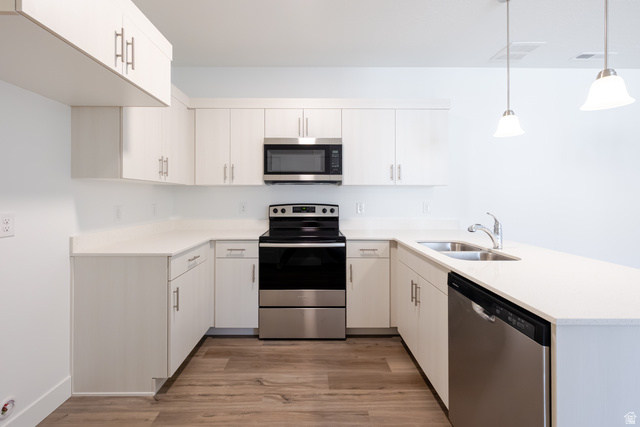 675 West 4500th South, Unit P204 Mapleton, UT 84664 - Photo 11 of 16 Modern kitchen featuring white cabinetry with brushed nickel hardware, white countertops, wood-finish flooring, stainless steel appliances, and pendant lighting