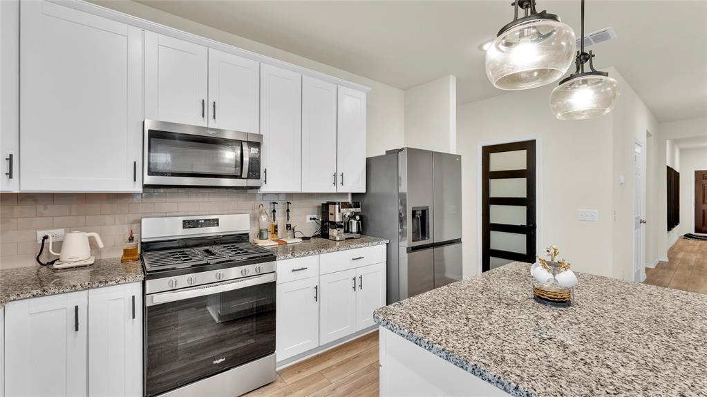 707 Indigo Road Princeton, TX 75407 - Photo 5 of 29 Modern kitchen featuring white shaker cabinetry, stainless steel appliances, speckled stone countertops, and a subway tile backsplash