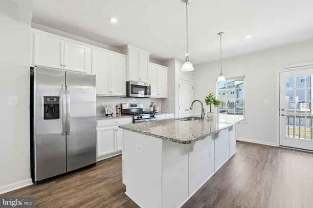 a kitchen with stainless steel appliances granite countertop a sink a stove a refrigerator and island with wooden floor