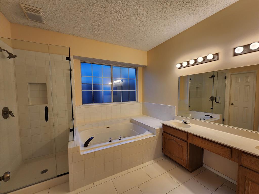 2413 Timber Ridge Lane Flower Mound, TX 75028 - Photo 13 of 32 Bathroom featuring a jetted soaking tub, a tiled shower with glass enclosure, a dual vanity with wood-finish cabinetry, a large wall mirror, and overhead lighting fixtures