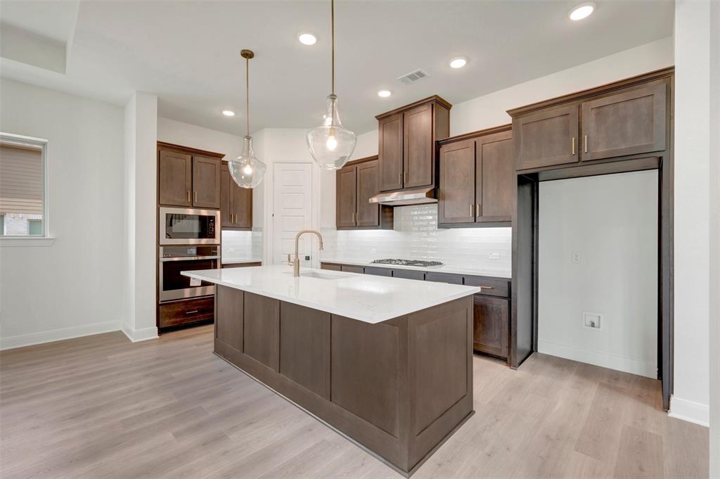 1908 Cola Drive Van Alstyne, TX 75495 - Photo 14 of 29 Modern kitchen featuring dark wood cabinetry, white subway tile backsplash, and light wood-finish flooring
