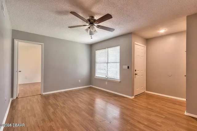 an empty room with wooden floor fan and windows