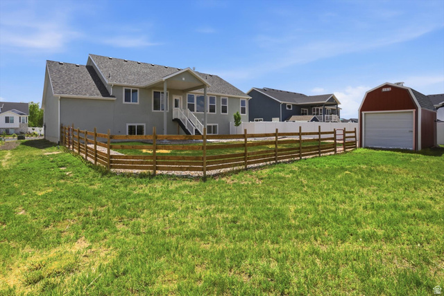 3636 West 910 South Syracuse, UT 84075 - Photo 62 of 70 Expansive backyard featuring a red barn-style shed with a garage door, a wooden split-rail fence, and a covered patio with white railings and stairs