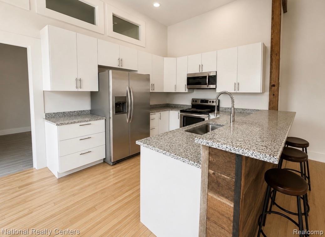 17 West Lawrence Street, Unit 2D Pontiac, MI 48342 - Photo 8 of 12 Kitchen featuring stainless steel appliances, white cabinetry, a granite countertop island with seating, wood-finish flooring, and a visible wood beam accent
