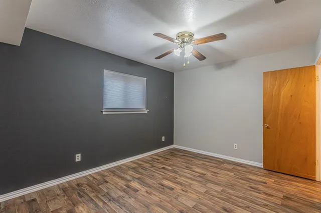a view of an empty room with wooden floor and a fan