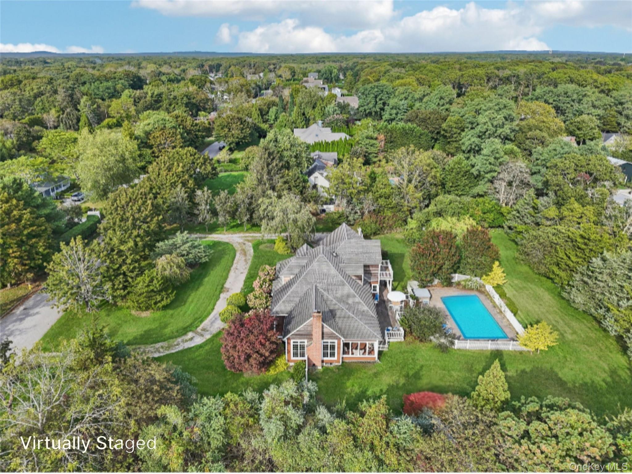 12 Laila Lane Remsenburg, NY 11960 - Photo 45 of 50 An aerial side perspective reveals the property’s architectural elegance, featuring a sunroom framed by floor-to-ceiling windows, and lushly landscaped grounds. Virtually Staged to Show open pool.