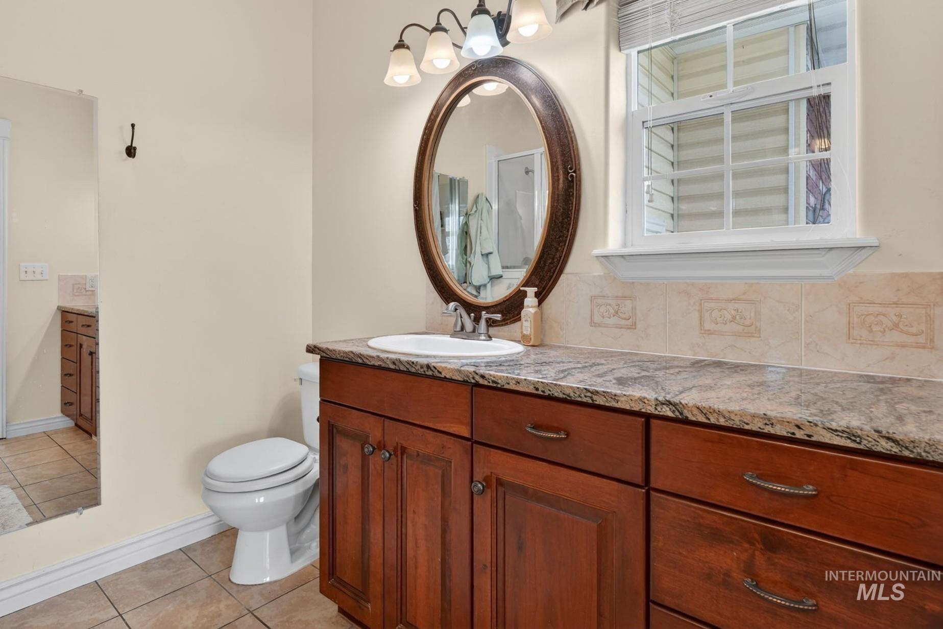 3352 Neeley Road American Falls, ID 83211 - Photo 18 of 43 Vanity area featuring a granite-style countertop, a rich wood-finish cabinet with storage, a white undermount sink, and an oval mirror