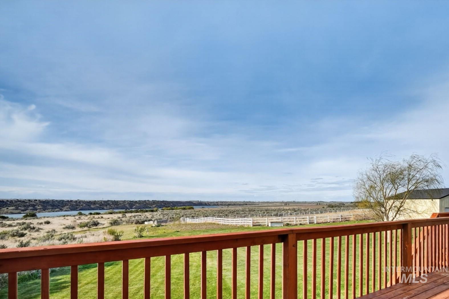 3352 Neeley Road American Falls, ID 83211 - Photo 7 of 43 Expansive outdoor deck featuring a wooden railing and decking, overlooking a green lawn, distant water, and natural landscape