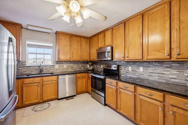 a kitchen with stainless steel appliances granite countertop wooden cabinets a sink a stove a dining table and chairs