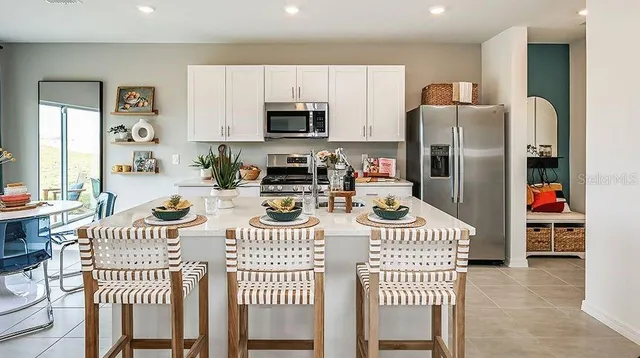 a kitchen with stainless steel appliances kitchen island granite countertop a refrigerator a stove top oven a dining table and chairs with wooden floor
