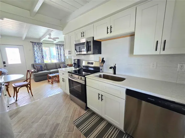 a kitchen with stainless steel appliances a stove a sink a refrigerator white cabinets and couches with wooden floor