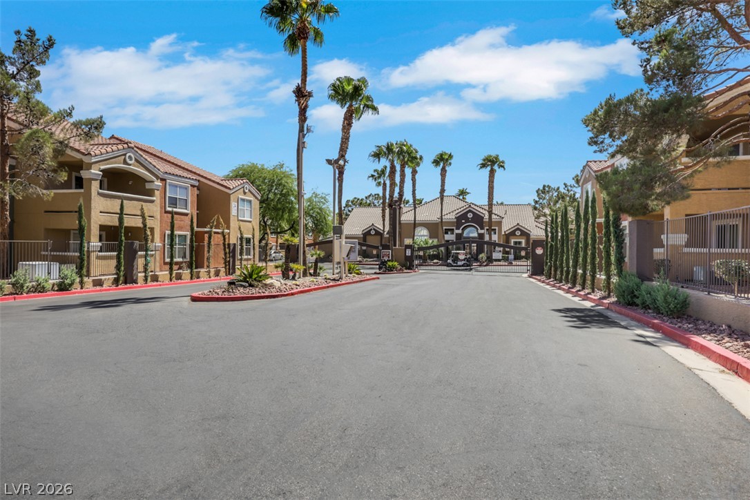 8101 West Flamingo Road, Unit 2136 Las Vegas, NV 89147 - Photo 1 of 32 Secure gated entry features stucco architecture and mature palm trees under a bright blue sky.