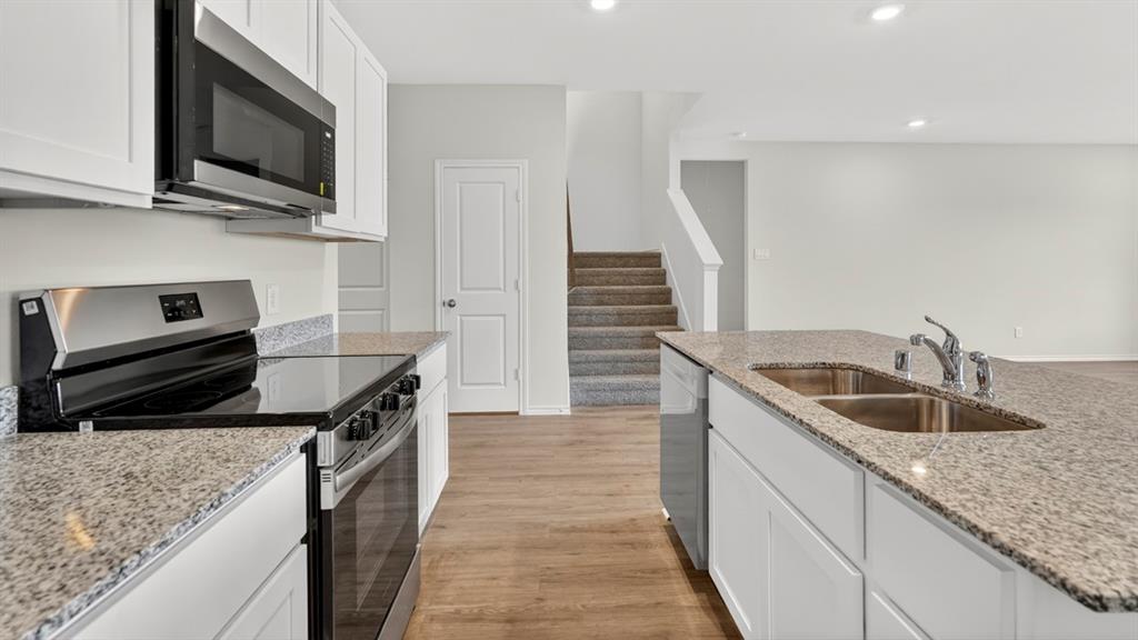 1683 Mantle Road Crandall, TX 75114 - Photo 6 of 31 Open-concept kitchen featuring an island with a double basin sink, stainless steel appliances, granite countertops, white cabinetry, and wood-finish flooring