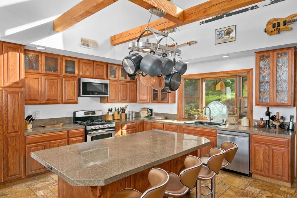 589 Anderson Road Alpine, CA 91901 - Photo 20 of 54 a kitchen with stainless steel appliances granite countertop a kitchen island a stove a sink dishwasher a dining table and chairs with wooden floor