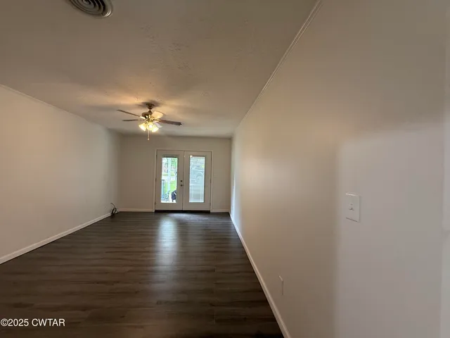 a view of an empty room with wooden floor and a ceiling fan