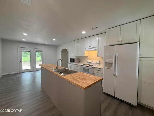 a kitchen with kitchen island a stove a refrigerator a sink and white cabinets with wooden floor