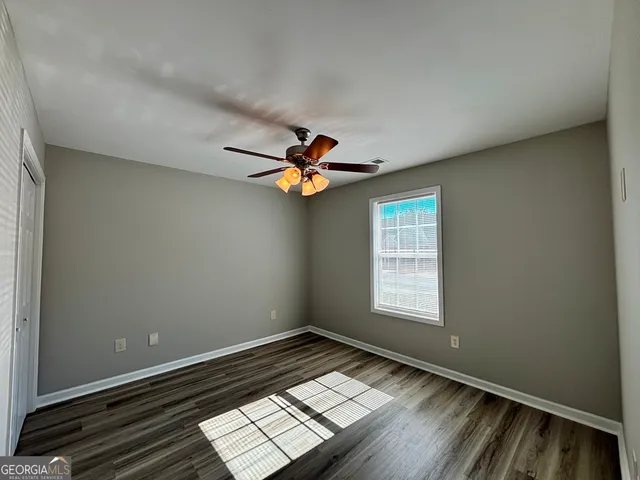 an empty room with wooden floor fan and windows