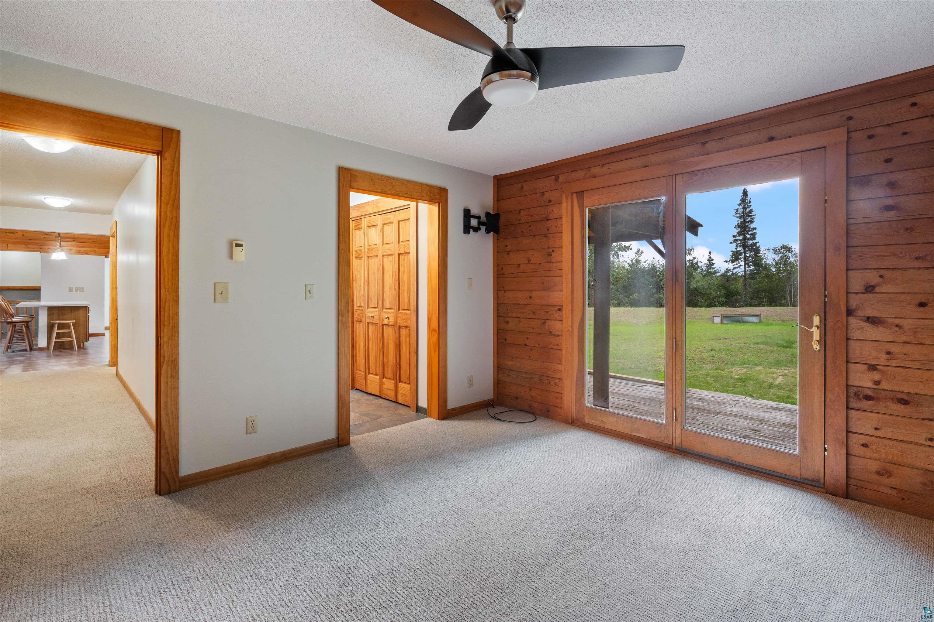 5373 Lester River Road Duluth, MN 55804 - Photo 15 of 39 Carpeted room with wood paneling, a ceiling fan, and glass paneled doors opening to an outdoor area