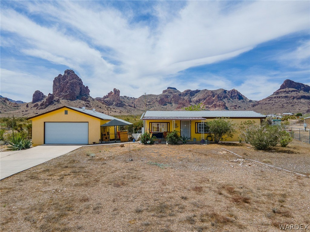 2465 Egar Road Golden Valley, AZ 86413 - Photo 62 of 98 The property features a single-story residence with a light yellow exterior, a covered front porch, and a detached garage
