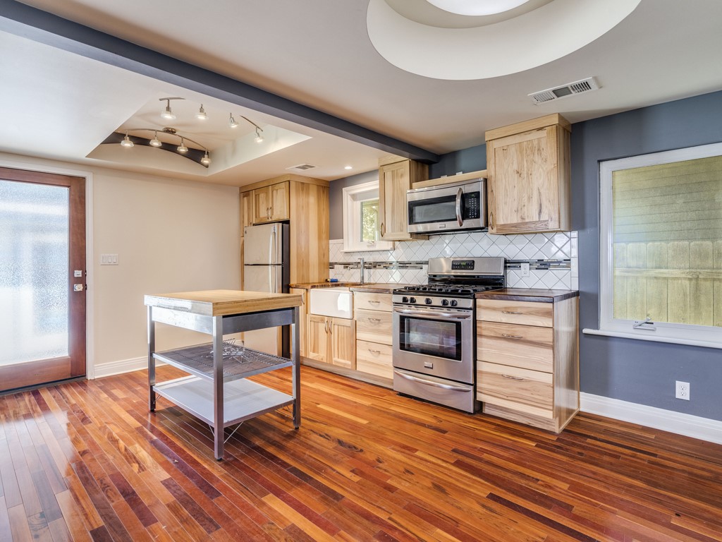 Kitchen with stainless steel appliances, light wood finish cabinetry, light wood-style flooring, dark countertops, and backsplash