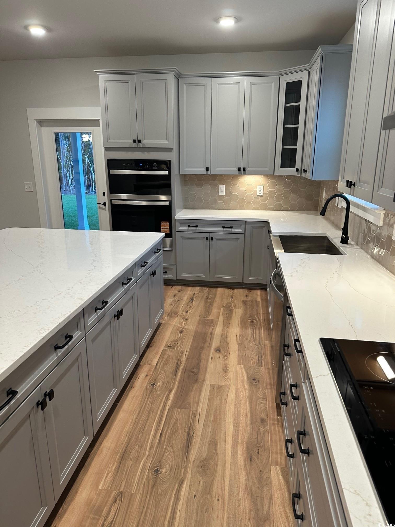 85 Northbrook Drive Murrells Inlet, SC 29576 - Photo 9 of 34 Kitchen with gray cabinets, decorative backsplash, glass insert cabinets, light stone countertops, and light wood-style floors