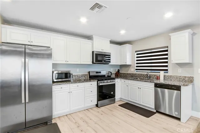 a kitchen with granite countertop a sink stainless steel appliances and white cabinets
