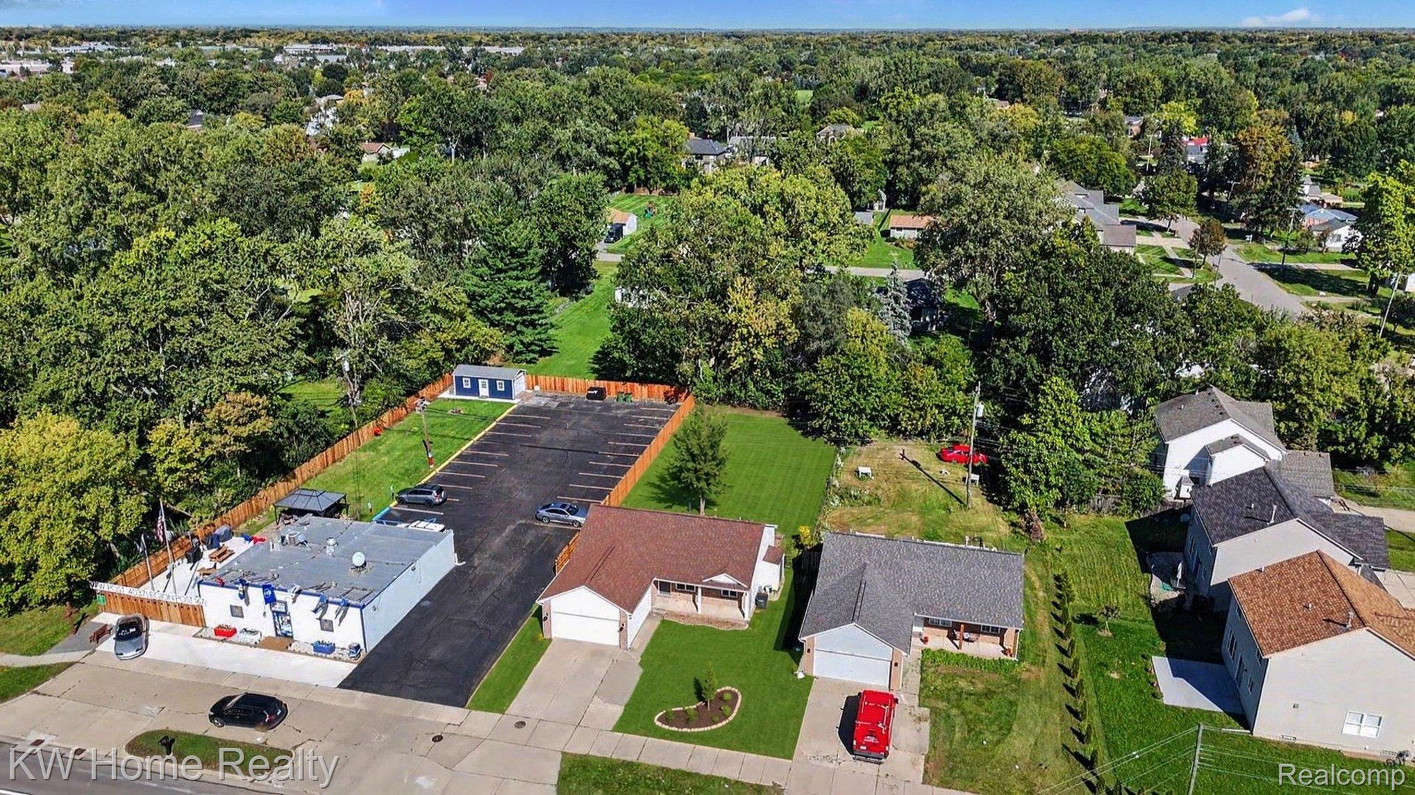 2383 East Maple Road Troy, MI 48083 - Photo 23 of 25 Expansive commercial lot with paved parking, a single-story building, and a separate storage shed, bordered by mature trees