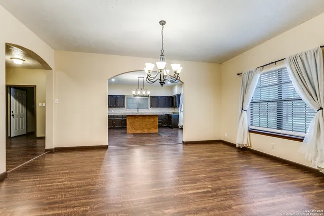 an empty room with wooden floor chandelier and windows