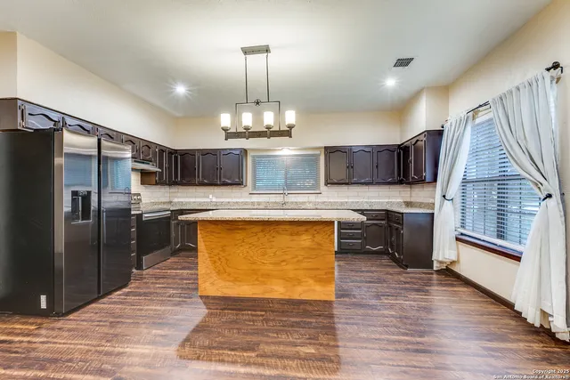 a kitchen with stainless steel appliances granite countertop a refrigerator a sink dishwasher a stove and a dining table with wooden floor