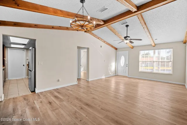 a view of an empty room with wooden floor and a ceiling fan