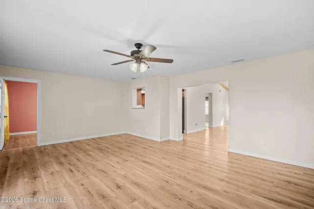 a view of an empty room with wooden floor and a ceiling fan