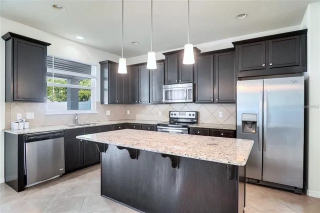 a kitchen with stainless steel appliances a sink a stove a refrigerator a center island and cabinets