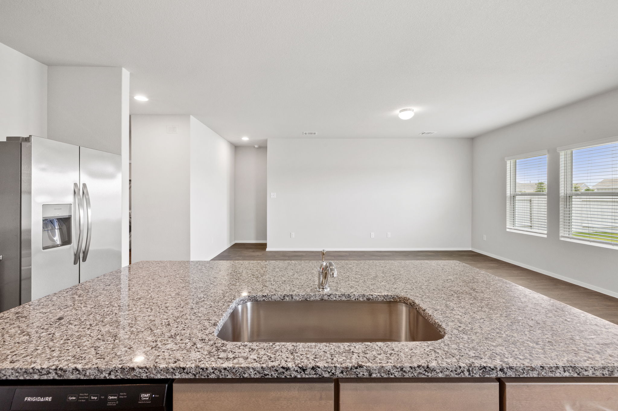 2460 Winding Creek Road Kyle, TX 78640 - Photo 6 of 20 A well-lit, open-concept kitchen features a spacious granite island with a stainless steel sink, flowing into a generous living area.
