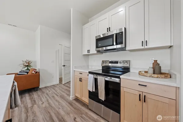 a kitchen with stainless steel appliances granite countertop a stove top oven a sink dishwasher and white cabinets with wooden floor