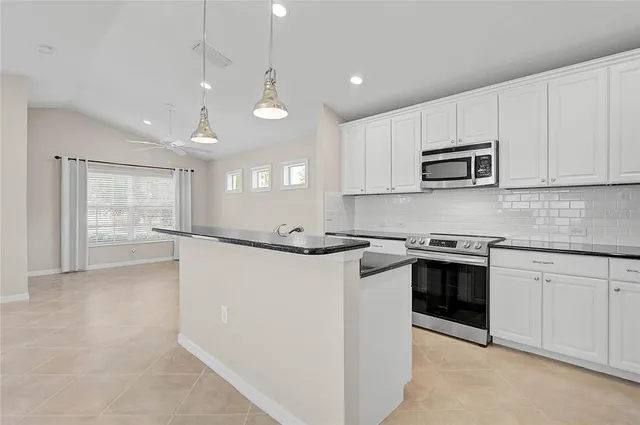 a kitchen with granite countertop a stove a sink a refrigerator and white cabinets with wooden floor