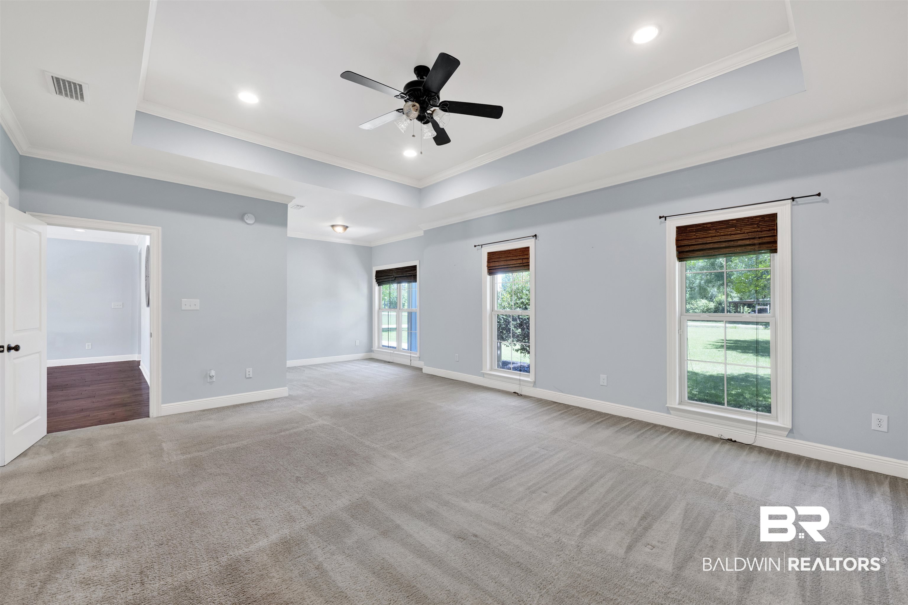 12944 Anna's Way Stapleton, AL 36578 - Photo 47 of 64 Spacious room featuring gray carpeting, a tray ceiling with recessed lighting and a ceiling fan, two windows with woven shades, and light blue wall paint