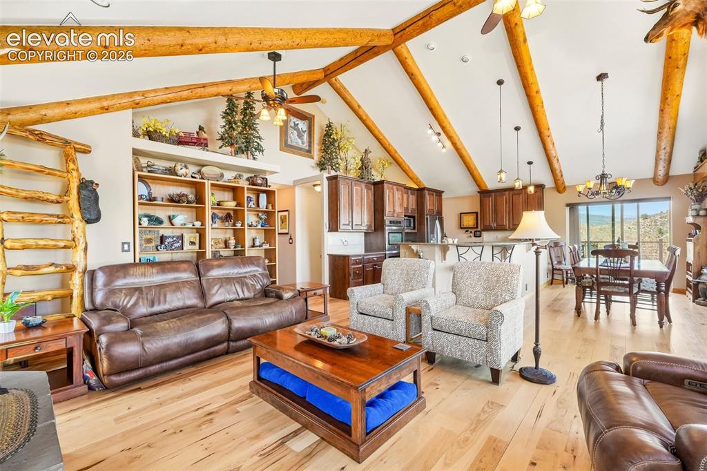 858 Oak Ridge Road Manitou Springs, CO 80829 - Photo 11 of 50 Open concept living room with tall vaulted-wood beamed ceilings, a wood burning fireplace, with a wall of windows giving you views of the mountains and city while bringing a nice touch of natural light inside , a walk out to the concrete wrap around deck all surrounded by solid hickory flooring