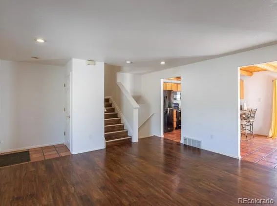 a view of an empty room with wooden floor and stairs