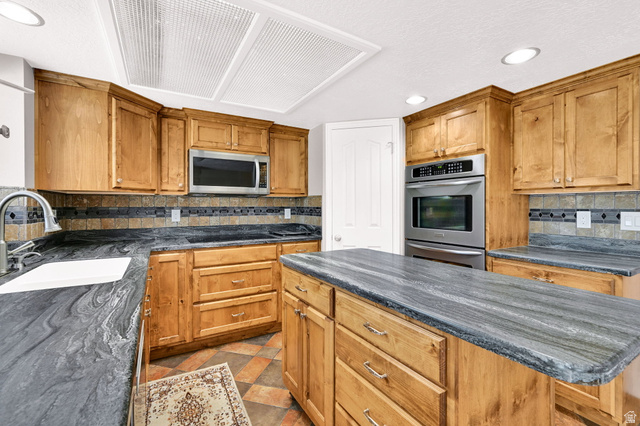4792 Glasmann Way South Ogden, UT 84403 - Photo 46 of 70 Kitchen featuring a large island with stone countertops, wood cabinetry, stainless steel appliances, and a tiled backsplash with electric or gas range top