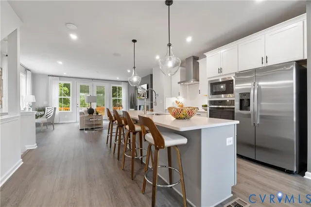 a kitchen with stainless steel appliances kitchen island granite countertop a refrigerator a stove a sink a dining table and chairs with wooden floor