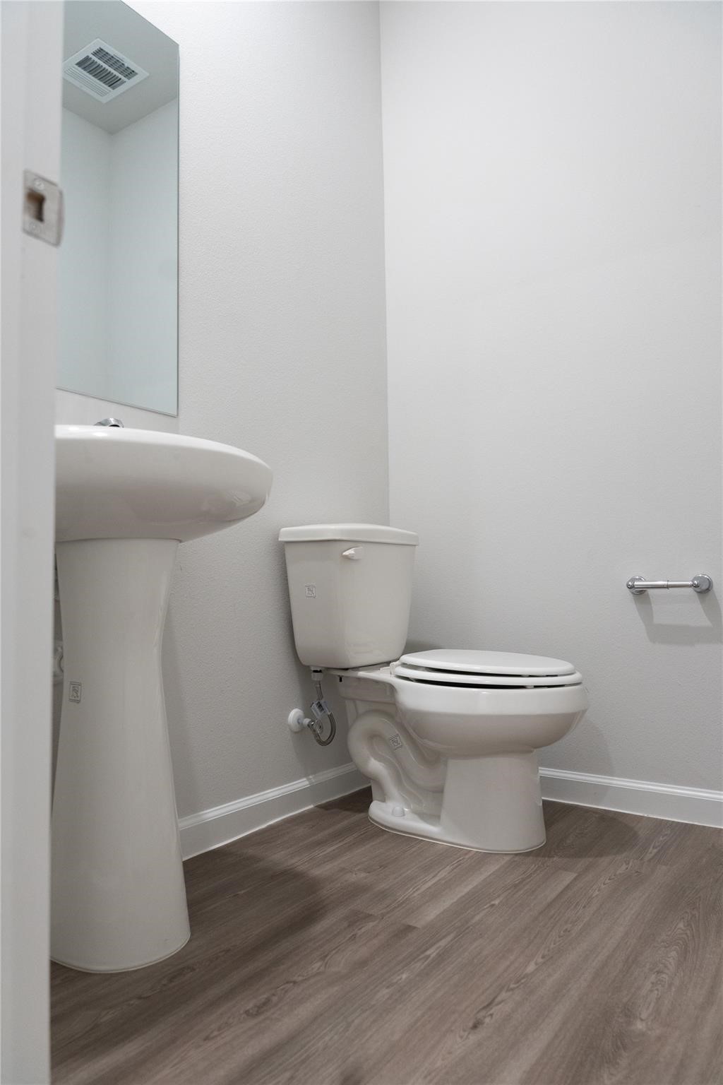 64 Valiant Ridge Trail Magnolia, TX 77354 - Photo 27 of 33 This is a compact half-bathroom with modern features. It includes a pedestal sink and a toilet, set against a neutral wall. The flooring is wood-style laminate, offering a clean and contemporary look.