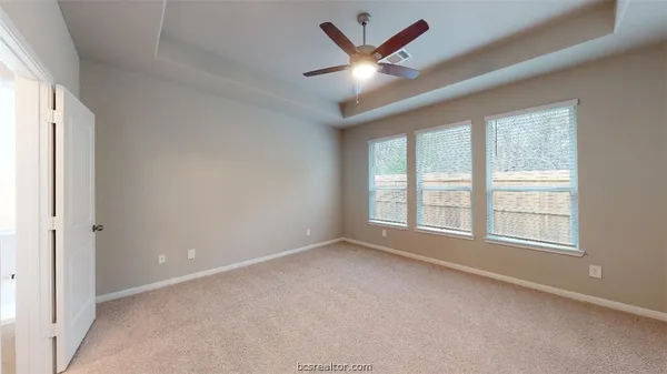 an empty room with chandelier fan and windows