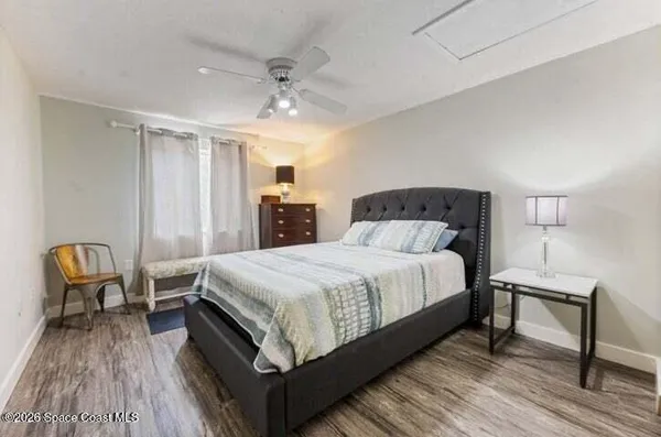 a bedroom with a bed a chair and potted plant on the dresser