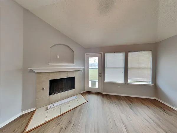 an empty room with wooden floor fireplace and windows
