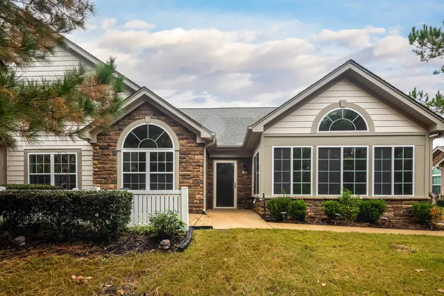 a view of a brick house with a yard plants and large tree