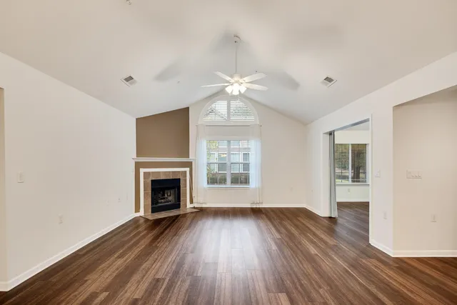 an empty room with wooden floor fireplace and windows