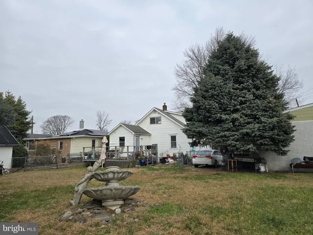 a view of a white house with a yard plants and large tree